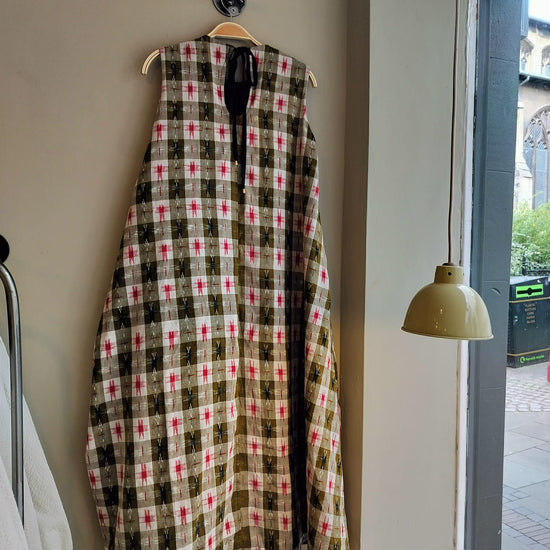 Plaid coat hanging on a hook against a wall with a window and lamp in the background.