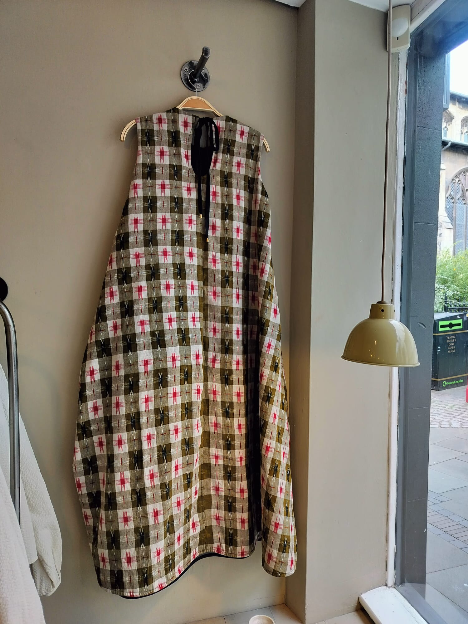Plaid coat hanging on a hook against a wall with a window and lamp in the background.