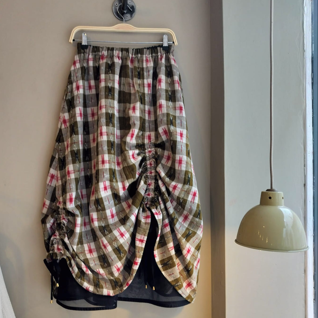 Plaid skirt hanging on a hook against a neutral wall with a lamp visible.