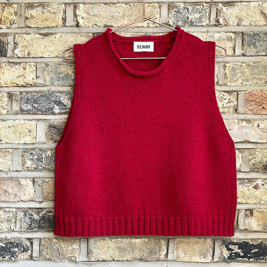 Red sweater vest on a hanger against a brick wall