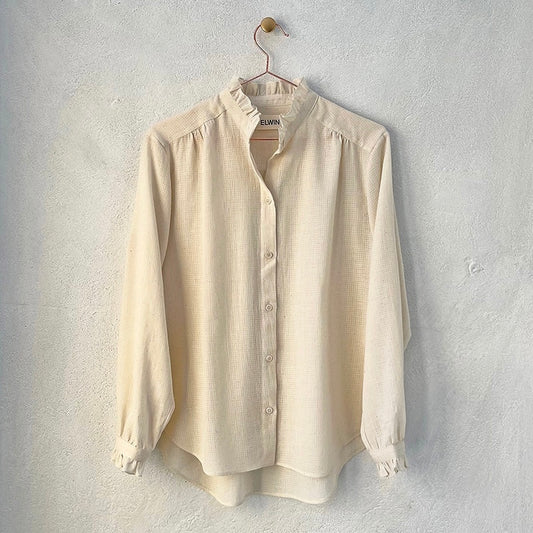 A beige, frill-shirt with a relaxed fit, displayed on a hanger against a neutral background.
