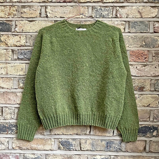 Green knitted sweater with a crew neck hanging against a brick wall.