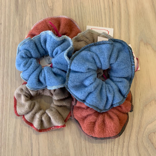 A collection of wool scrunchies in various colors including blue, beige, and red, displayed on a wooden surface.