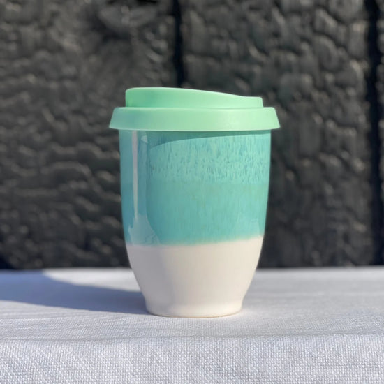 Turquoise and white ceramic cup with a green lid on a textured surface