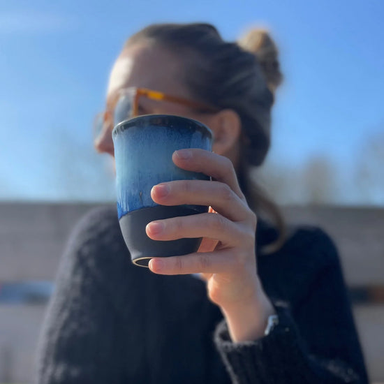 Person holding a blue cup outdoors with a blurred background