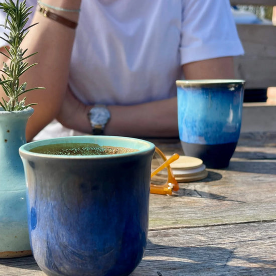 Blue ceramic mug on a wooden table with a person sitting in the background