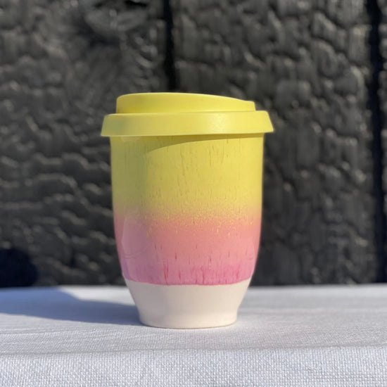 Gradient yellow to pink reusable cup on a textured surface with a dark background