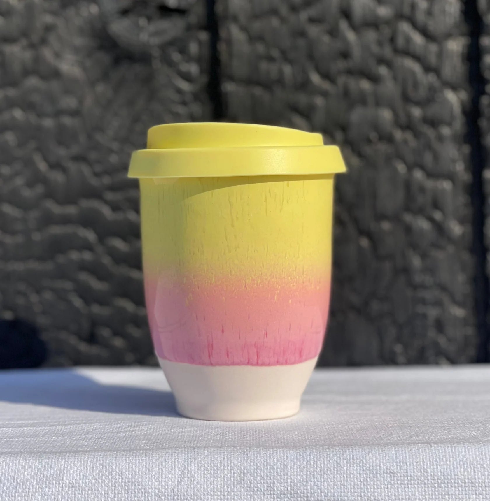 Gradient yellow to pink reusable cup on a textured surface with a dark background