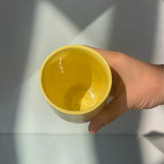 Hand holding a yellow ceramic cup against a light background