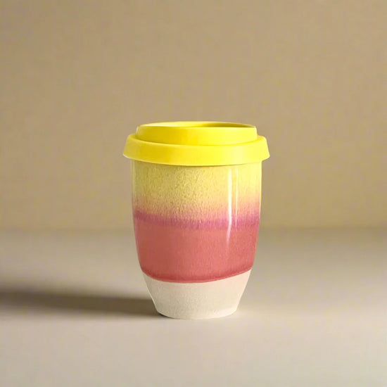 Colorful ceramic cup with a yellow lid on a beige background