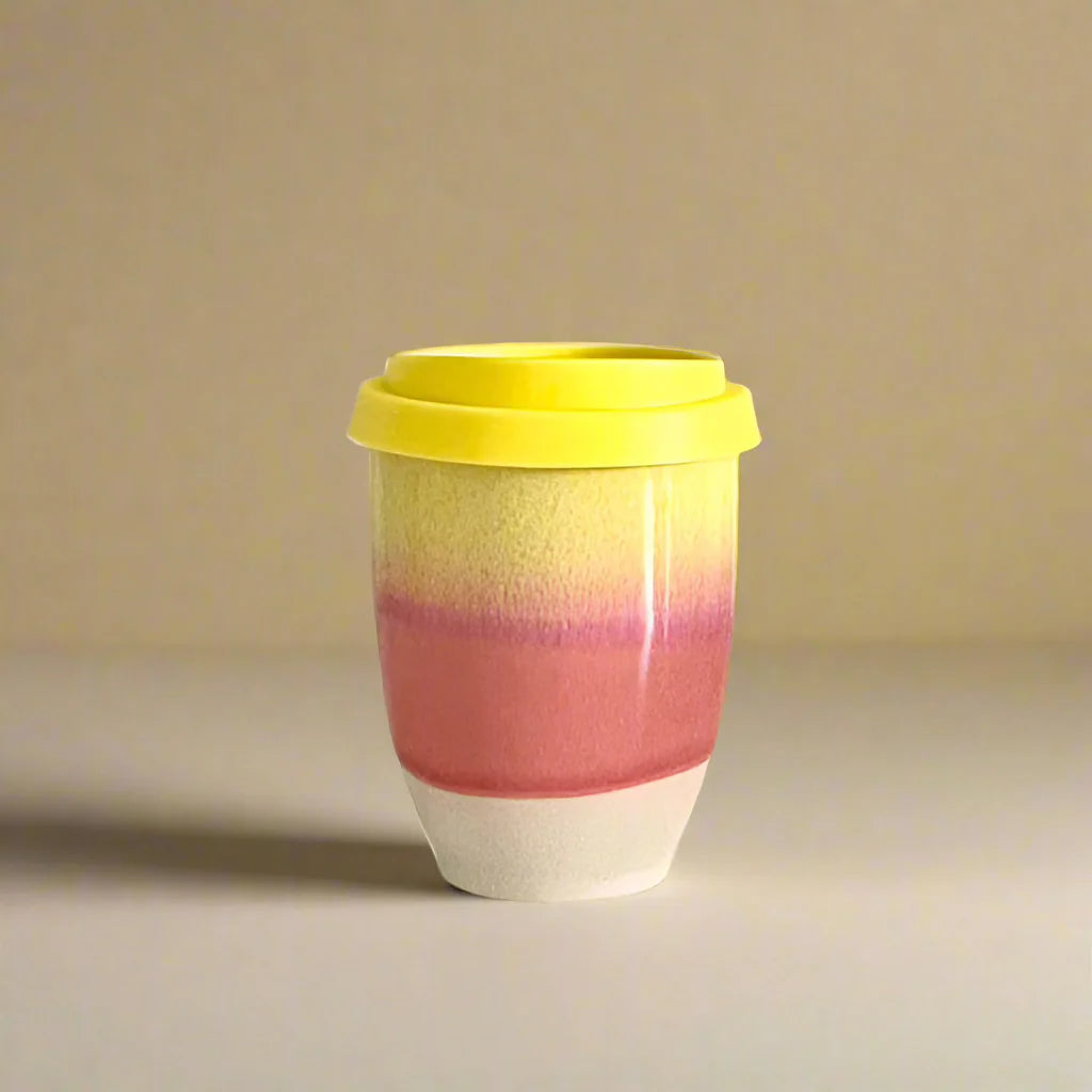 Colorful ceramic cup with a yellow lid on a beige background