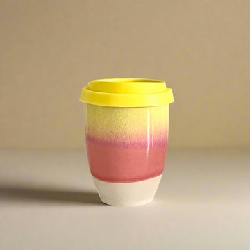 Colorful ceramic cup with a yellow lid on a beige background