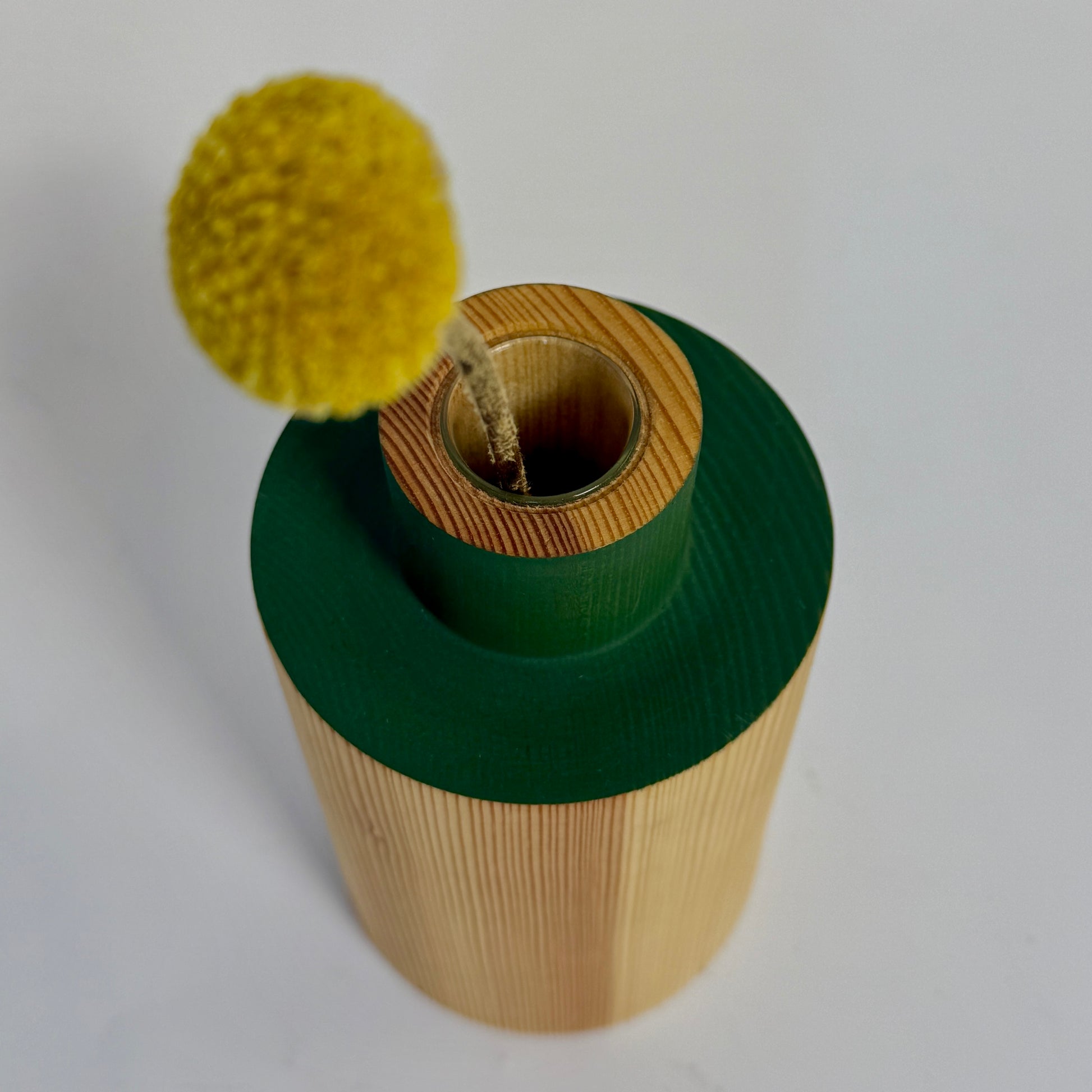 Wooden cylindrical object with a green top and yellow ball on a white background