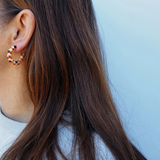 checkered brown and beige acetate hoop earrings with surgical steel posts on human with brown long hair