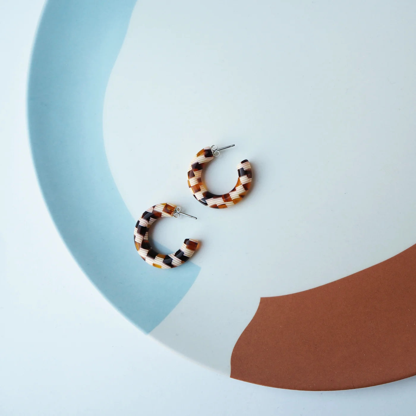 checkered brown and beige acetate hoop earrings with surgical steel posts on a blue and brown background
