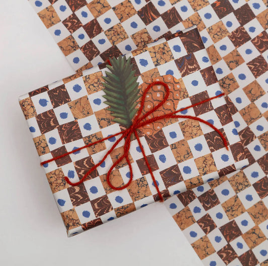 Gift wrapped in patterned paper with red string and a green leaf on a white background