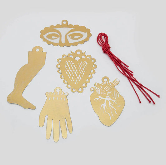 Gold metal charms shaped like a foot, hand, heart, and anatomical heart on a white background with red string.