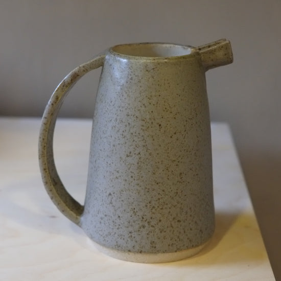 Speckled grey ceramic pitcher on a light surface with a neutral background