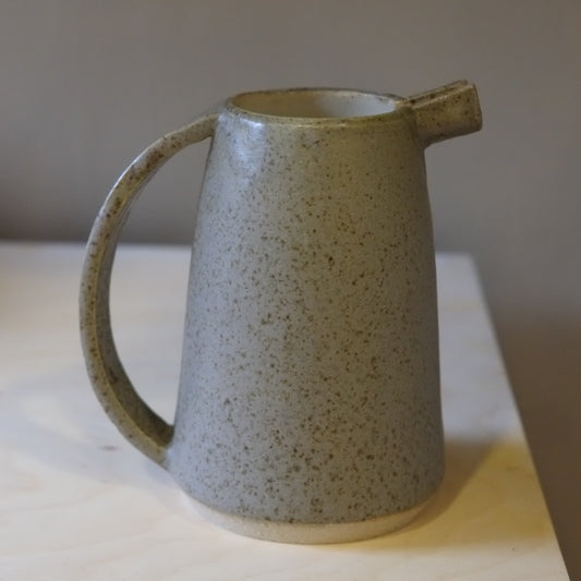 Speckled grey ceramic pitcher on a light surface with a neutral background