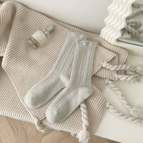Pair of light gray socks with tassels on a textured surface