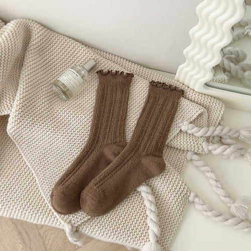 Pair of brown socks on a textured surface with a bottle of lotion.