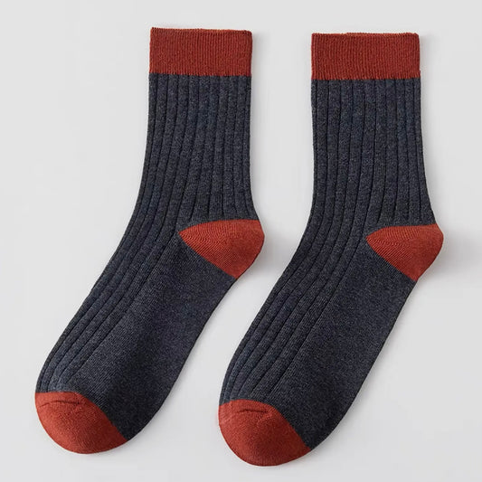 Pair of dark grey socks with rust-colored tops and toes on a light grey background