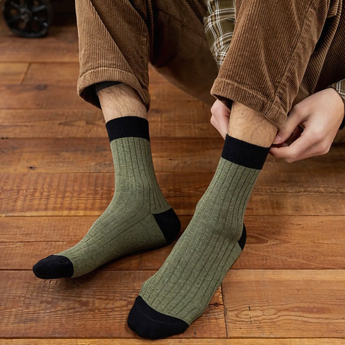 Person wearing green socks with black toes and cuffs on a wooden floor with brown cord trousers