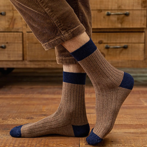 Brown socks with blue accents on the toe and cuff worn by a person on a wooden floor in front of a wooden dresser