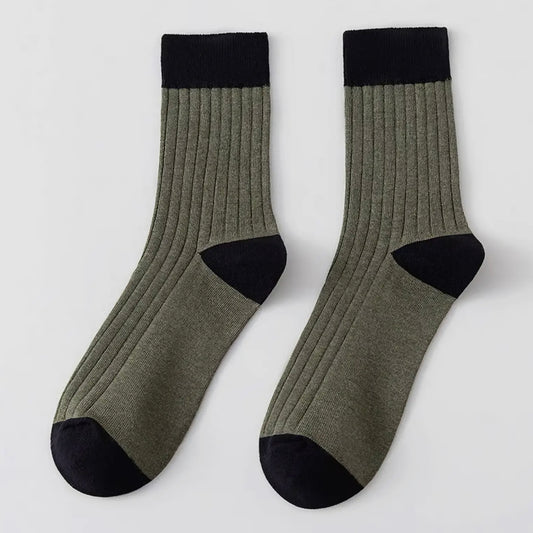 Pair of green socks with black toes and cuffs on a light grey background