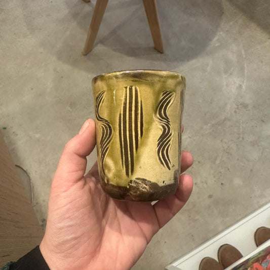 Hand holding a decorative glass container with gold and black patterns on a concrete floor.
