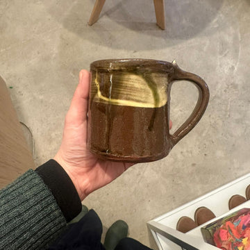 Hand holding a brown ceramic mug with a blurred background