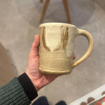 Hand holding a ceramic mug outdoors on a concrete surface