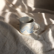 Load image into Gallery viewer, Ceramic mug with blue design on a textured beige surface
