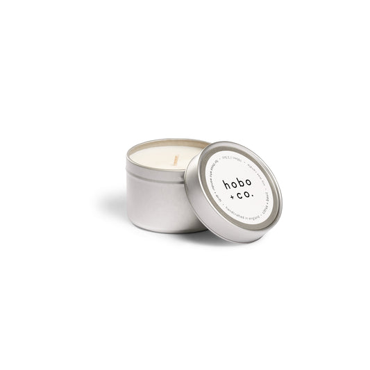 Candle in a metallic tin with 'hobo + co.' label on a white background