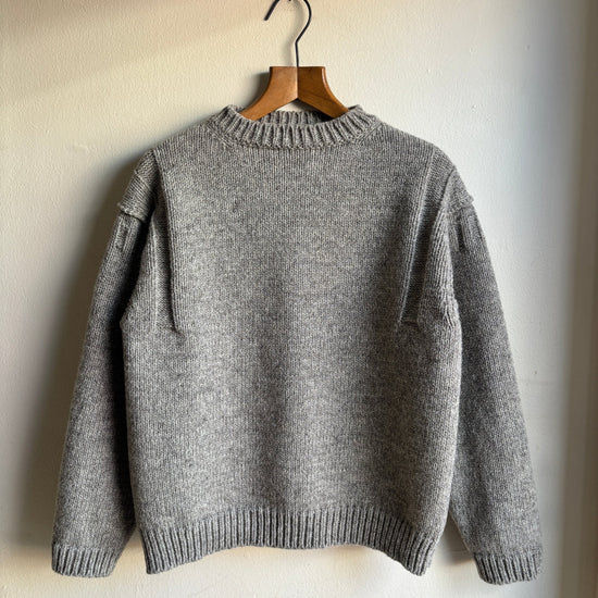 A gray knit sweater hanging on a wooden hanger against a plain off-white wall.