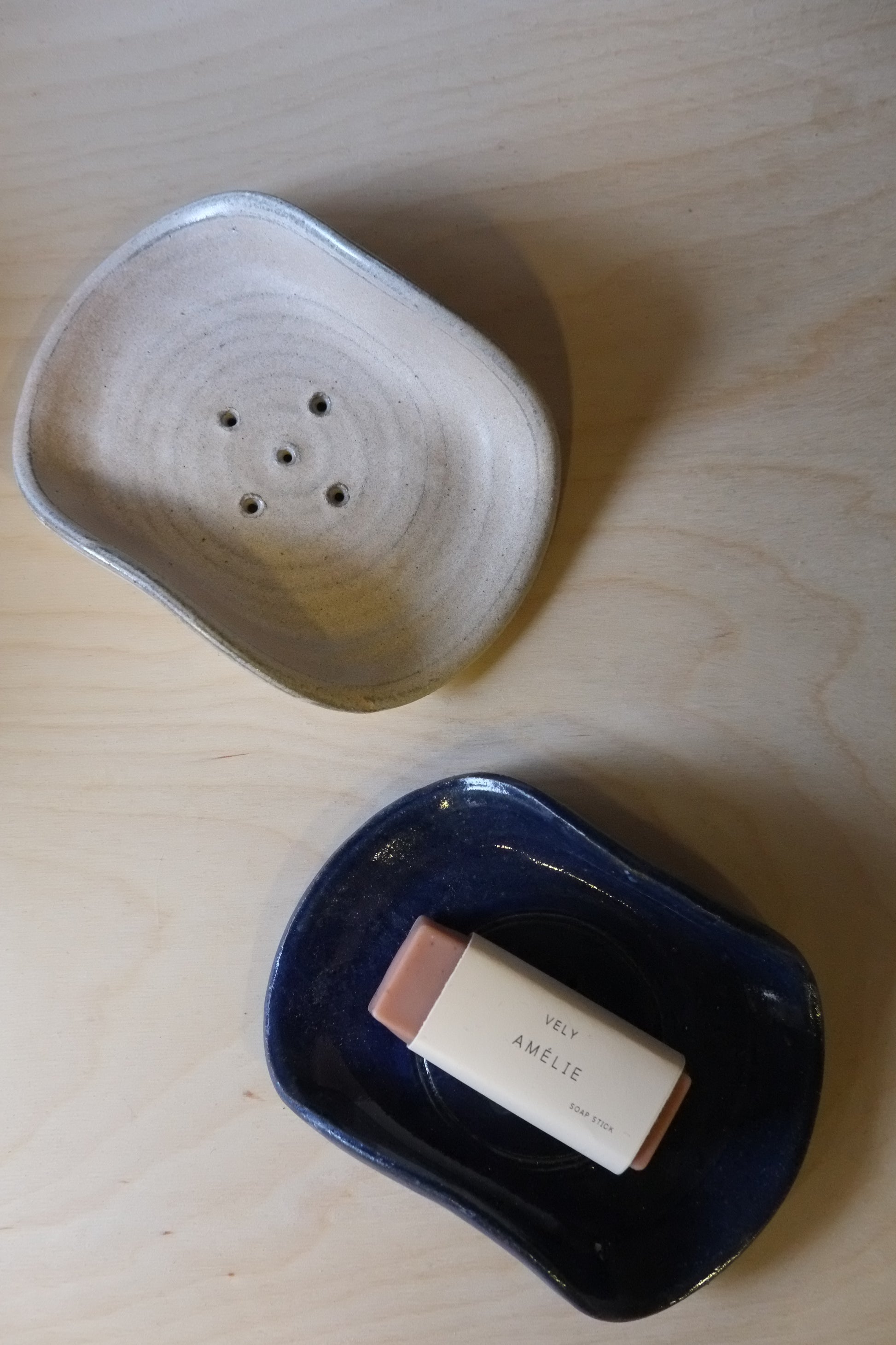 Two ceramic containers on a light wood surface, one with a bar of soap inside.