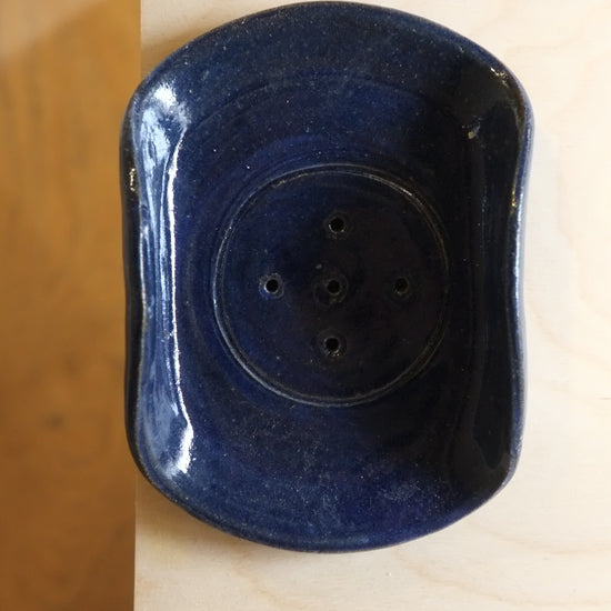 Blue soap dish with multiple holes on a wooden surface