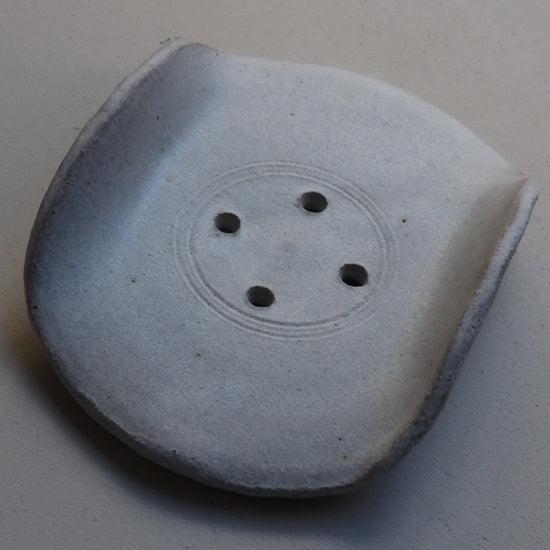 A single ceramic soap dish, a central circular recess, and four small dark holes, photographed on a plain light background.