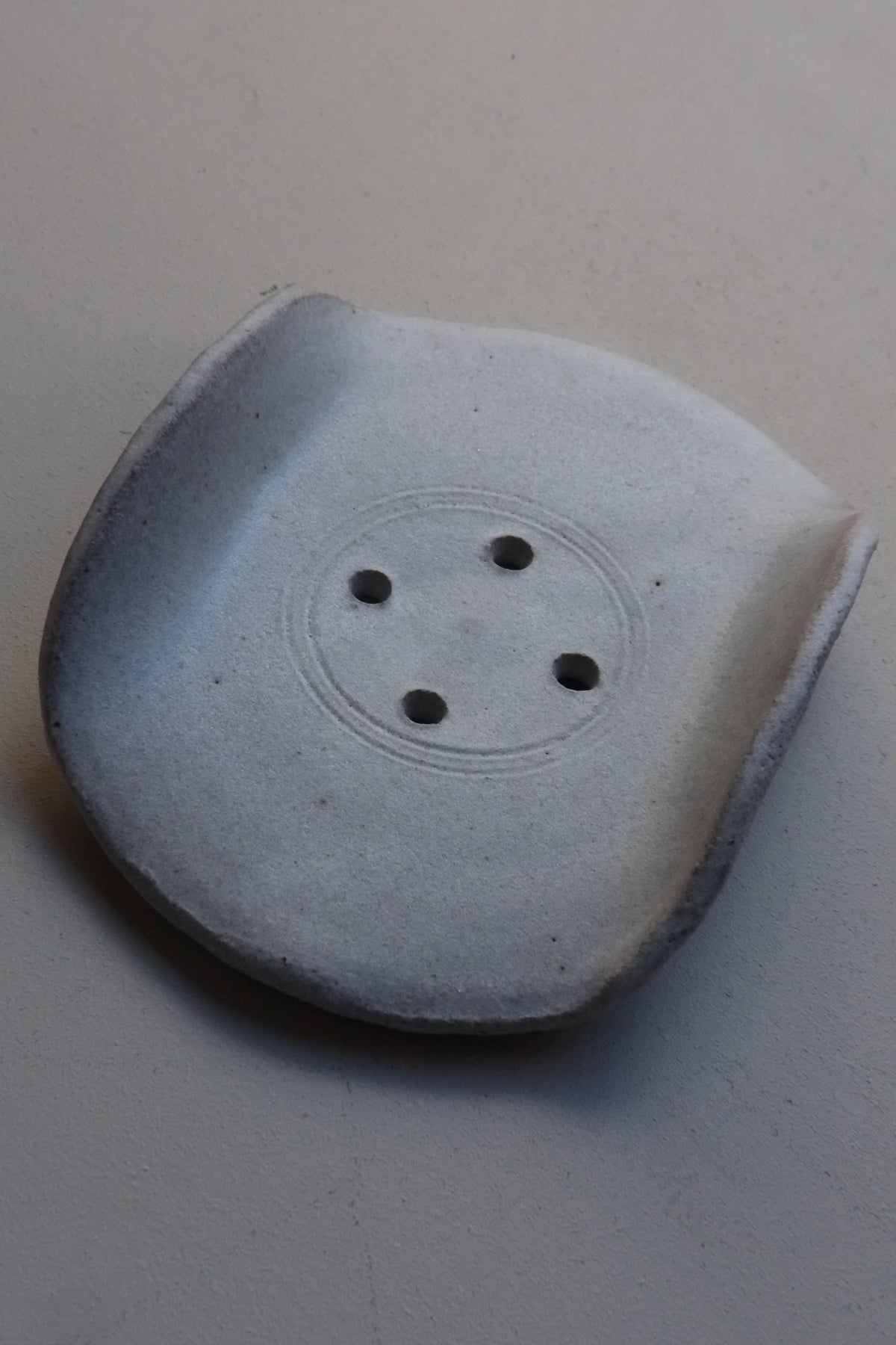 A single ceramic soap dish, a central circular recess, and four small dark holes, photographed on a plain light background.