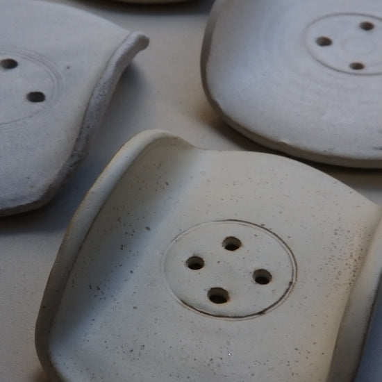 Four handmade ceramic soap dishes with a textured, speckled off-white glaze, arranged on a neutral light gray background.