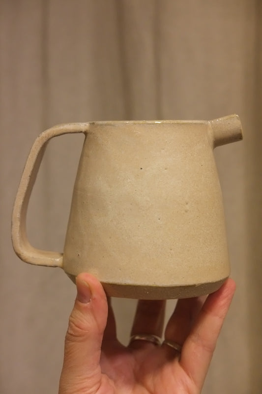 plaster pink ceramic short jug held by hand against a beige curtain
