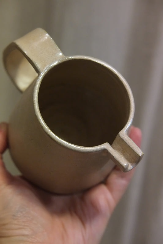 top of a ceramic jug in colour plaster pink held by a hand against a beige curtain