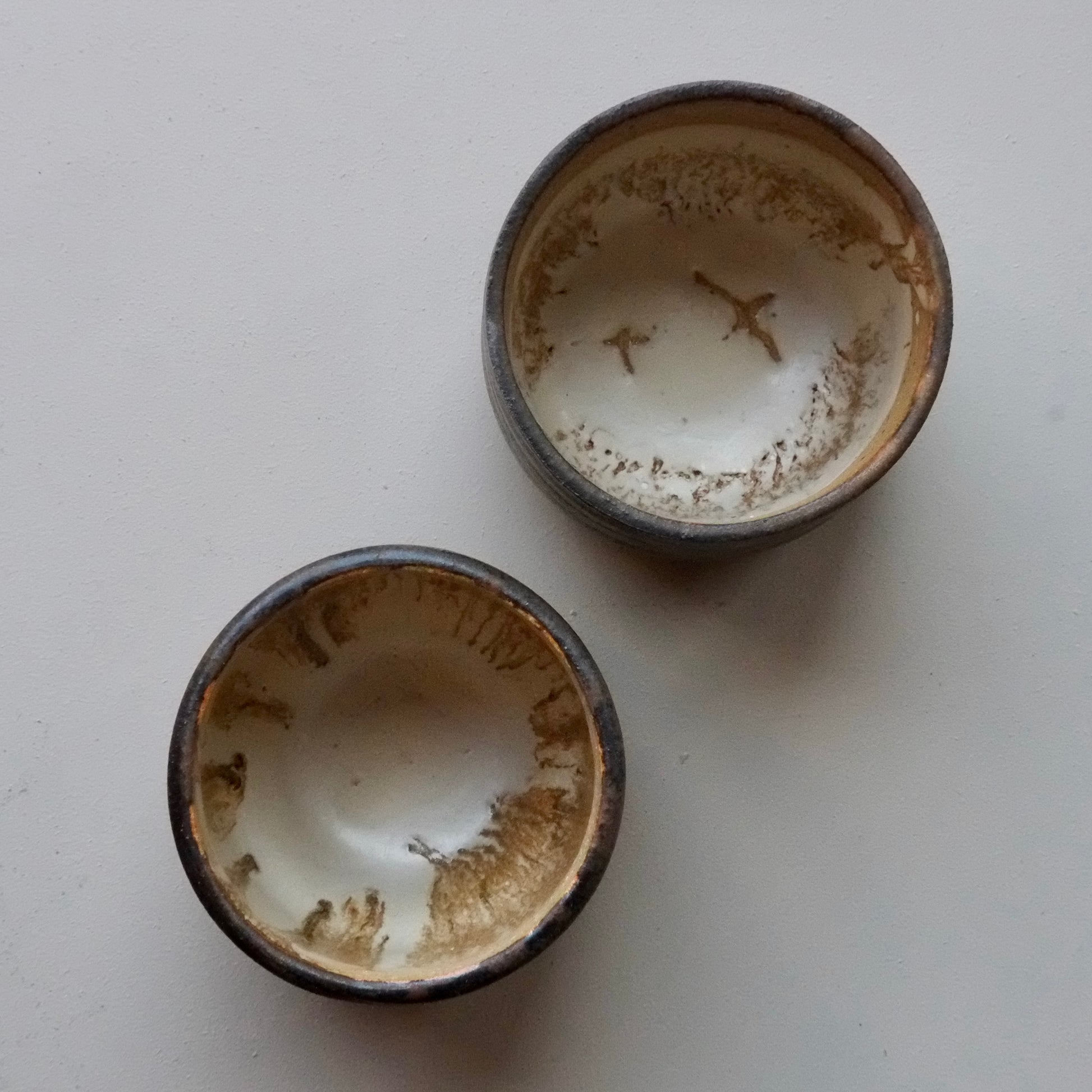 Two small handmade ceramic bowls with a rustic finish, showing a cream-colored interior with brown speckled and chipped detailing, set against a plain off-white background.