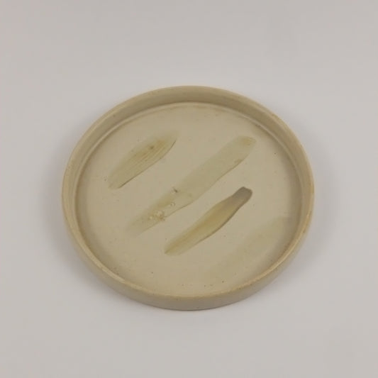 Round beige object with cut-out design on a light gray background