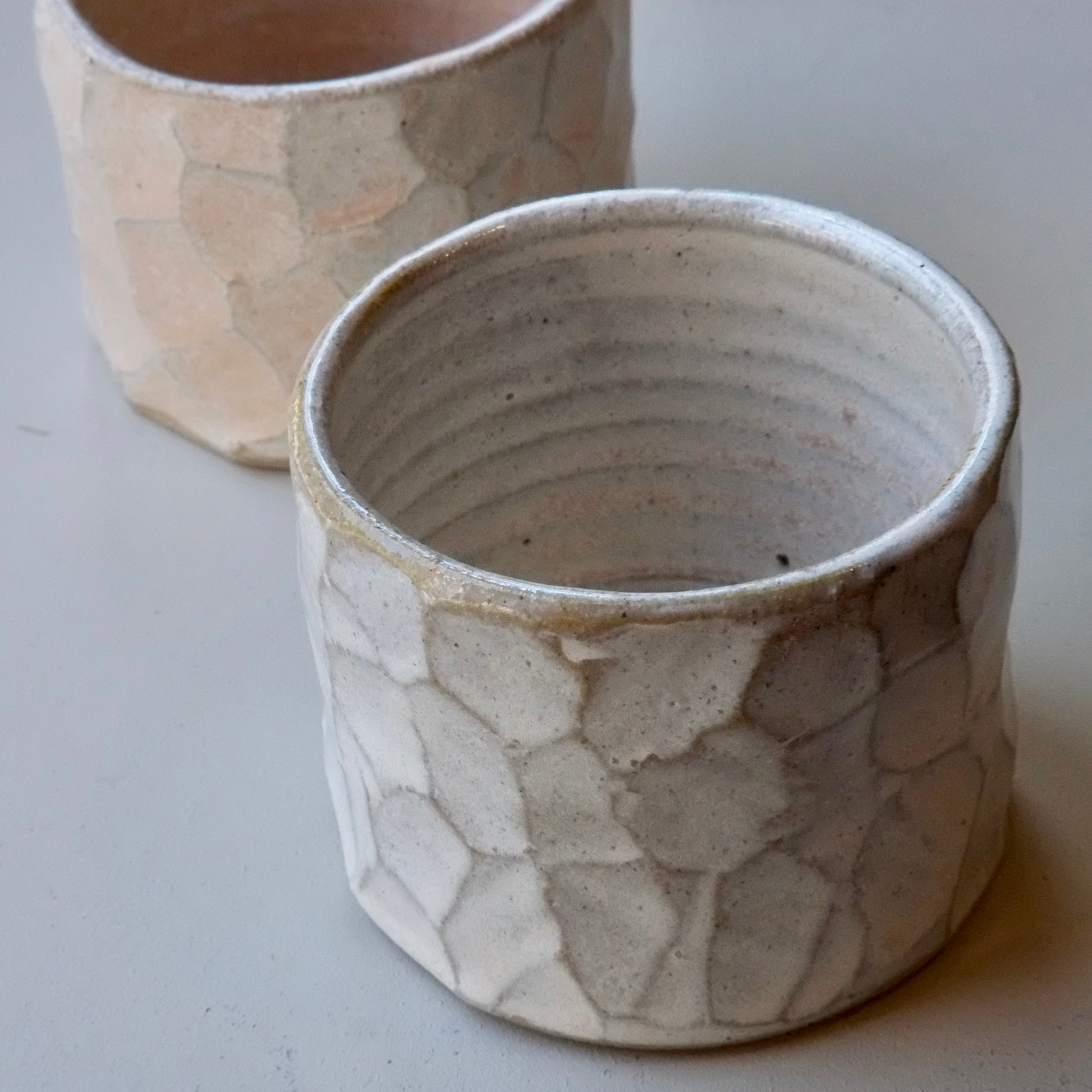 Two handmade ceramic pots with a textured, organic crackle glaze pattern in off-white and beige tones, shown on a neutral light gray background.