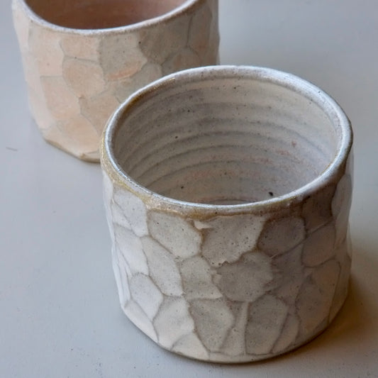 Two handmade ceramic pots with a textured, organic crackle glaze pattern in off-white and beige tones, shown on a neutral light gray background.