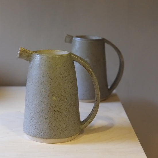 Two ceramic pitchers on a wooden surface with a neutral background