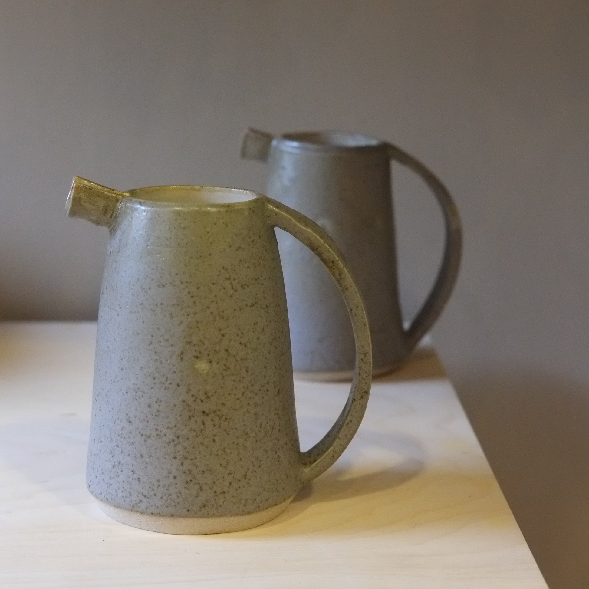 Two ceramic pitchers on a wooden surface with a neutral background