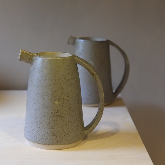 Two ceramic pitchers on a wooden surface with a neutral background
