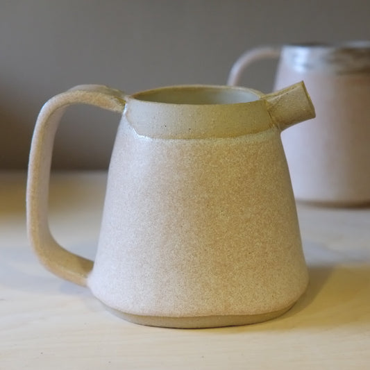 Beige ceramic pitcher on a wooden surface with a blurred background